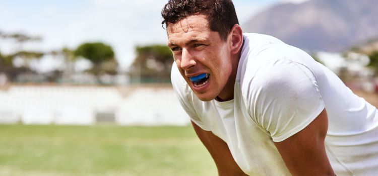 A man wearing a blue boil-and-bite mouthguard during outdoor sports training