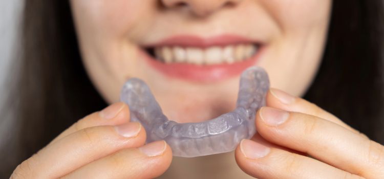 Woman holding a clear night guard for teeth grinding relief and bruxism protection.