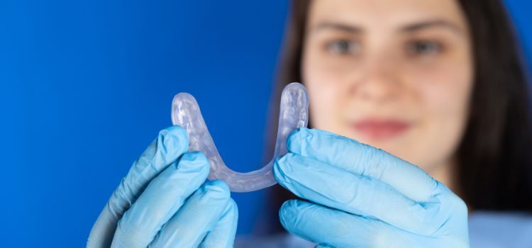 Female dentist wearing gloves holding a clear custom night guard against a blue background