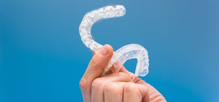 Hand holding a clear dental night guard against a blue background