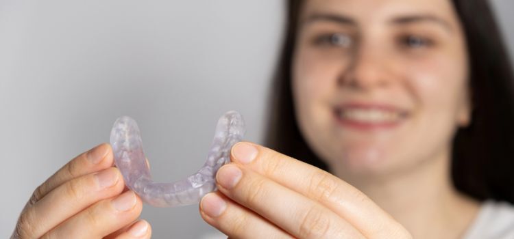 Smiling woman holding a clear dental night guard for bruxism relief