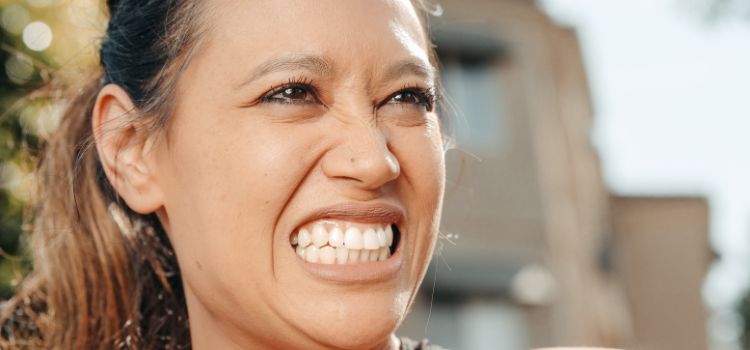 Woman clenching her teeth tightly outdoors, possibly experiencing stress-related bruxism