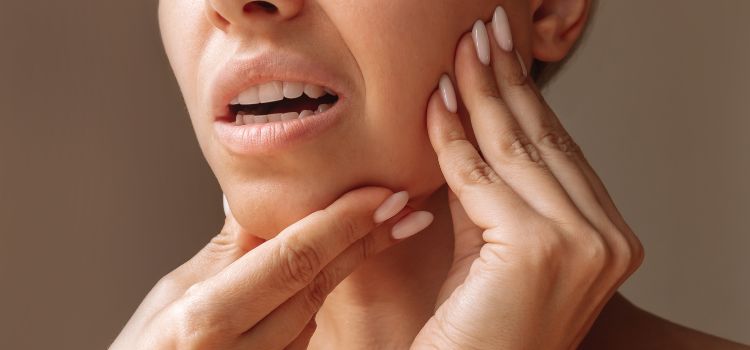 An image of a woman holding her cheek and jaw due to pain and misalignment.