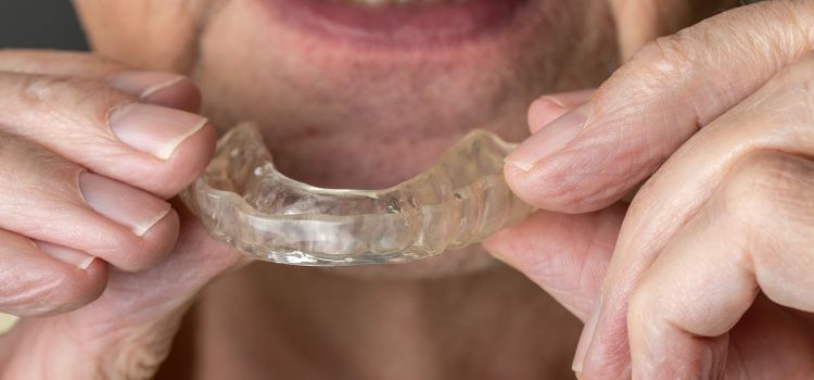 Elderly man inserting a clear night guard into his mouth