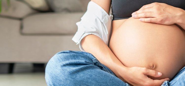 Close-up of a pregnant woman sitting on the floor, gently cradling her belly with both hands