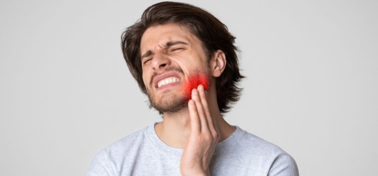 A man with visible jaw pain and red highlight on his cheek, showing signs of bruxism or muscle tension.