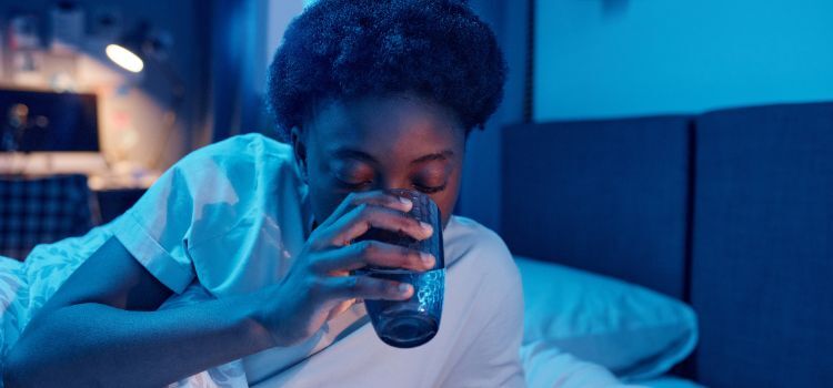 Woman drinking water at night in bed — increased nighttime thirst may be linked to dry mouth caused by a night guard.