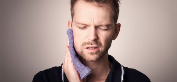 A man holding his jaw with a towel due to tooth sensitivity or pain possibly linked to cavities