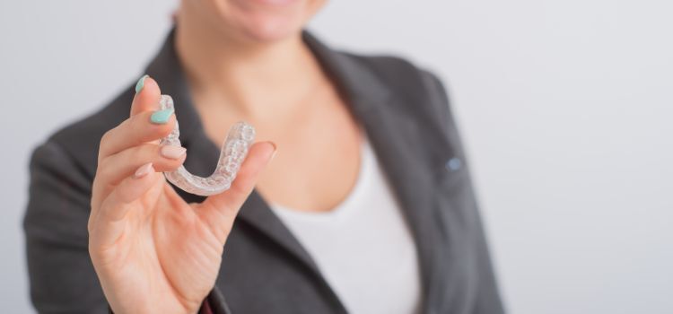 Happy woman in a blazer holding a clear dental night guard with a smile
