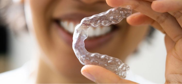 Smiling woman holding a clear custom night guard for bruxism relief